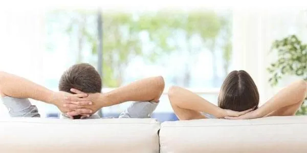Couple or roommates looking out window while laying against couch.