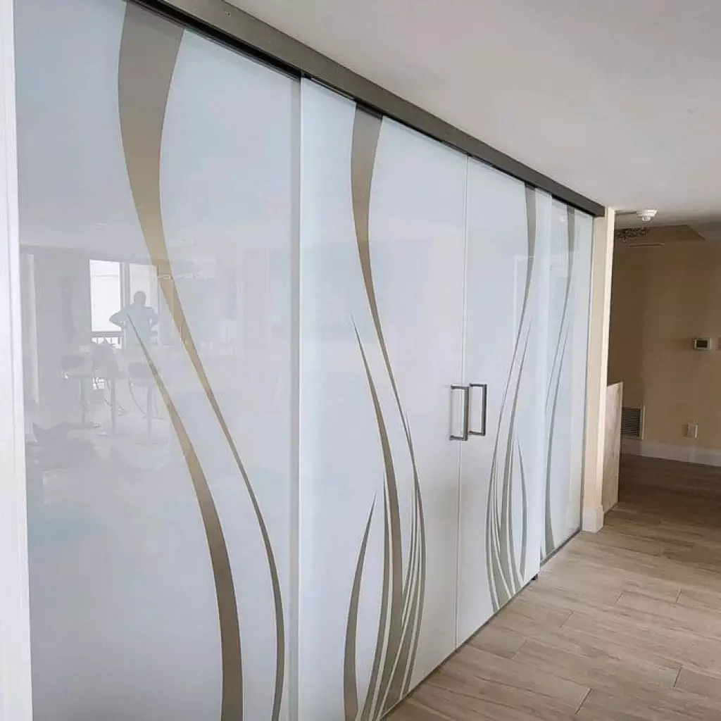 20230707_145412 Frosted glass sliding doors with curved beige lines and 3M decorative film separate a hallway from a living area with light wood flooring and neutral walls.