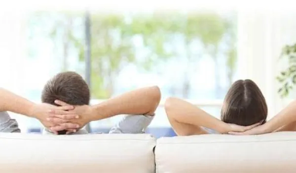Couple or roommates looking out window while laying against couch.