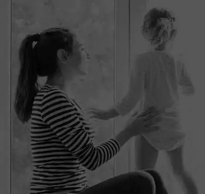 testimonial-mobile Toddler standing and looking out window while steadied by mother.
